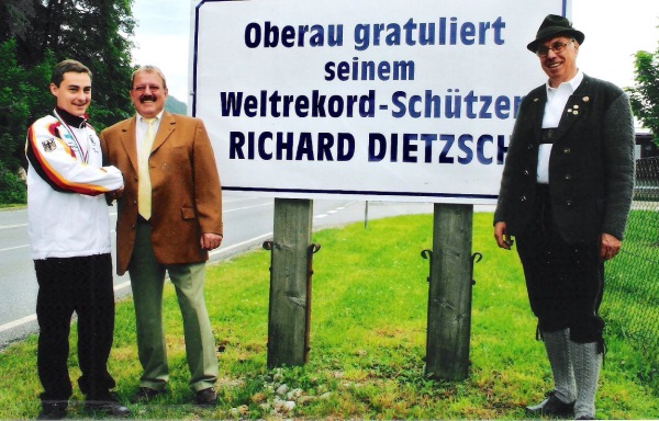 Foto Richard Dietzsch mit B&uuml;rgermeister Imminger und 1. Sch&uuml;tzenmeister Hans Huber am Ortsschild mit Gratulationstafel zum Weltrekord